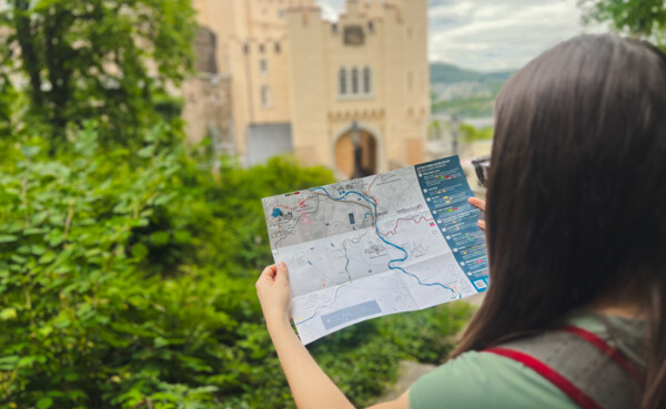 Frau steht vor Schloss Stolzenfels und blickt auf einer Broschüre ©Ryne & Denise Cook