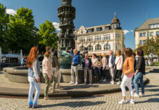 Stadtführung vor Historiensäule am Görresplatz. Menschengruppe hört dem Stadtführer zu. ©