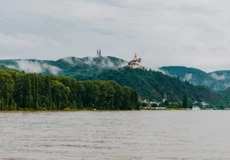 Blick auf die Marksburg vom Rheinufer umgeben von Bergen und Wald mit dem Rhein im Vordergrund