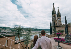 Pärchen von Hinten im Paradiesgarten blickt auf die Türme des Schloss Stolzenfels ©Koblenz-Touristik GmbH, Philip Bruederle