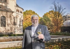 Lächelnder Stadtführer Michael Hörter mit einem Glas Wein in der Hand steht vor dem Basilika St. Kastor im Herbst © Koblenz-Touristik GmbH, Picture Colada