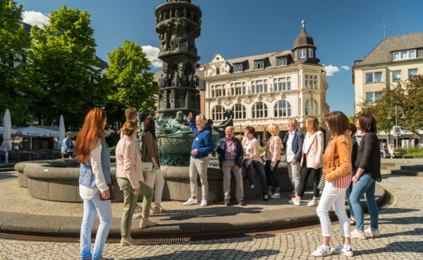 Stadtführung vor Historiensäule am Görresplatz. Menschengruppe hört dem Stadtführer zu.