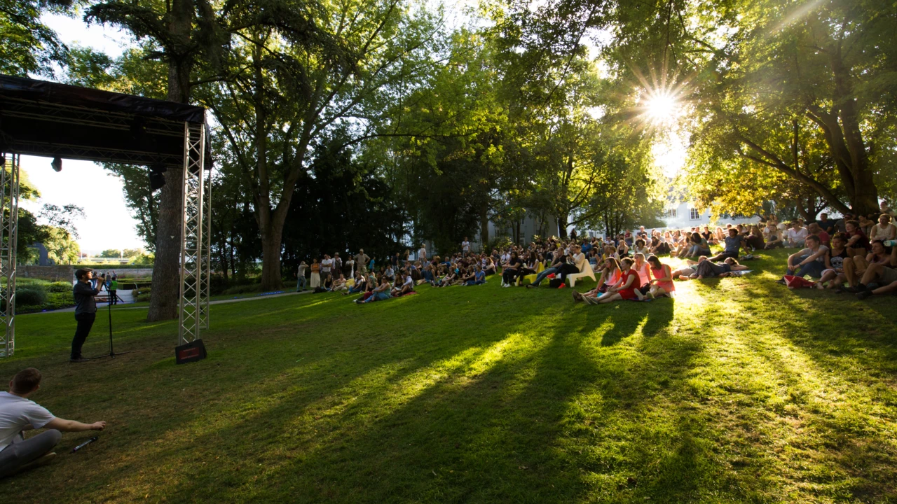 Menschengruppen sitzen auf dem Rasen im Schlosspark und hören einen Dichter zu
