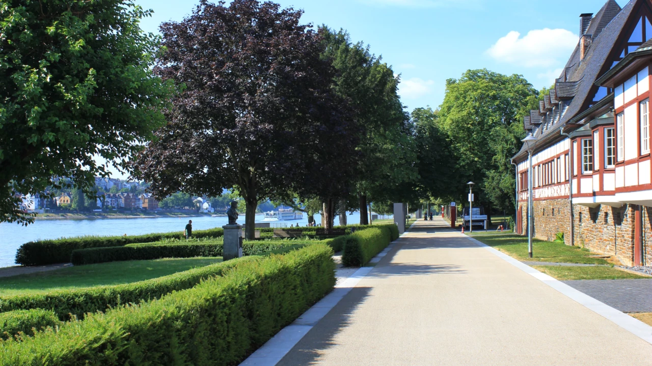 Spazier- und Fahrradweg vor dem Weindorf an den Rheinanlagen umgeben von Statuen, Hecken und Bäumen