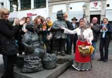 Verkleidete Stadtführerin mit Korb und Gemüse lacht mit einer Führungsgruppe vor Figuren auf dem Münzplatz © Koblenz-Touristik GmbH, Juraschek