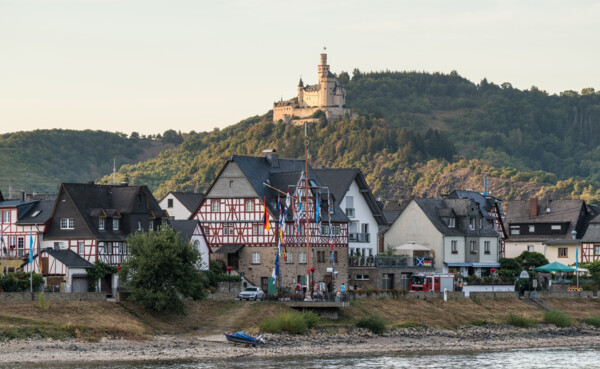 Blick auf die Marksburg, umgeben von Wald, im Vordergrund der Rhein und Fachwerkhäuser ©Dominik Ketz