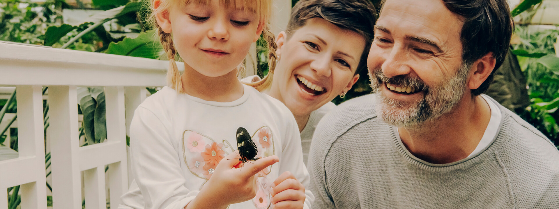 Familie im Schmetterlingsgarten in Sayn lachen während Tochter einen Schmetterling auf ihrem Finger beobachtet ©Koblenz-Touristik GmbH, Philip Bruederle