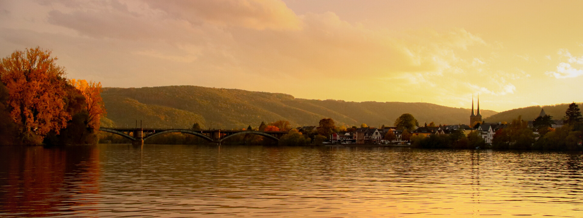 Blick über die Mosel bei Sonnenuntergang, im Hintergrund ein kleiner Ort mit Kirchturmspitze ©Johannes Bruchhof Blick über die Mosel bei Sonnenuntergang, im Hintergrund ein kleiner Ort mit Kirchturmspitze ©Johannes Bruchhof