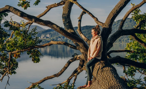 Dame von Seite blickt auf den Sonnenaufgang bei Maria Laach mit dem Kloster und See im Hintergrund