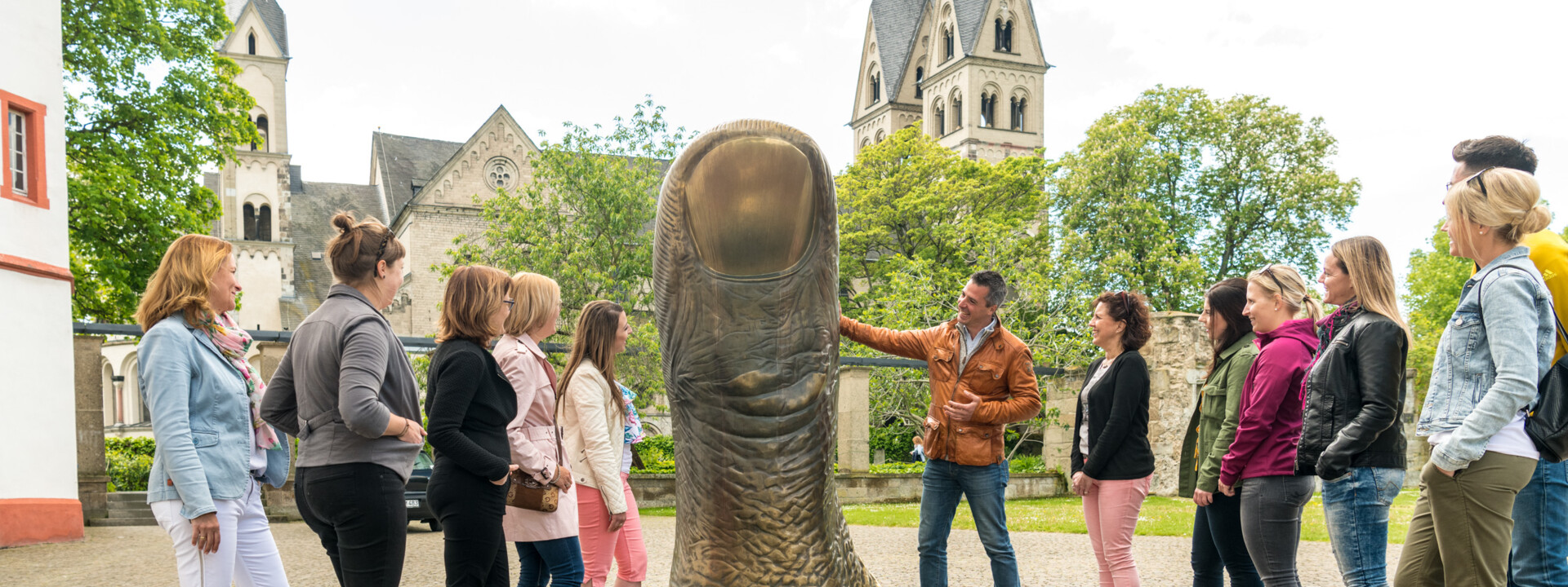 Reisegruppe hört einem Stadtführer zu, während er eine große Daumenstatue vor dem Ludwigmuseum erklärt ©Koblenz-Touristik GmbH, Dominik Ketz