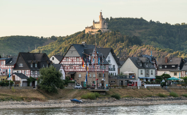 Blick auf die Marksburg, umgeben von Wald, im Vordergrund der Rhein und Fachwerkhäuser ©Dominik Ketz