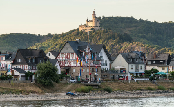 Blick auf die Marksburg, umgeben von Wald, im Vordergrund der Rhein und Fachwerkhäuser © Dominik Ketz