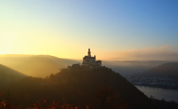 Die Marksburg auf einer Höhe mit Rhein und benebelten Bergen beim Sonnenuntergang ©