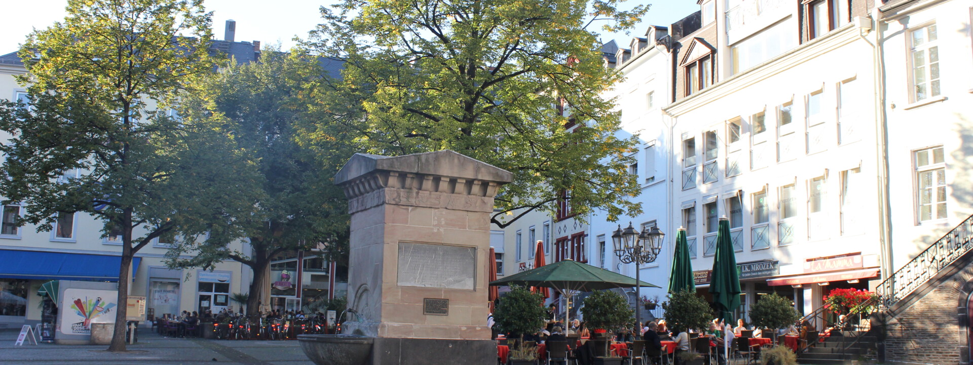 Brunnen auf dem Platz "Am Plan" in Koblenz mit Cafés und Bäumen im Hintergrund ©Koblenz-Touristik GmbH