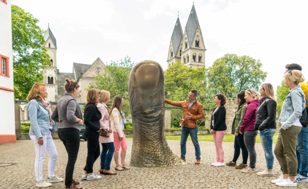 Reisegruppe Stadtführer Daumstatue Basilika St. Kastor Deutschherrenhof Koblenz © Koblenz-Touristik GmbH, Dominik Ketz Reisegruppe hört einem Stadtführer zu, während er eine große Daumenstatue vor dem Ludwigmuseum erklärt © Koblenz-Touristik GmbH, Dominik Ketz
