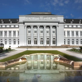 Kurfürstliches Schloss in Koblenz von der Vorderseite, die Säulen spiegeln sich in einer Wasserfläche im Vordergrund