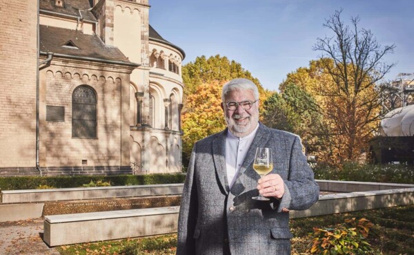 Lächelnder Stadtführer Michael Hörter mit einem Glas Wein in der Hand steht vor dem Basilika St. Kastor im Herbst ©Koblenz-Touristik GmbH, Picture Colada