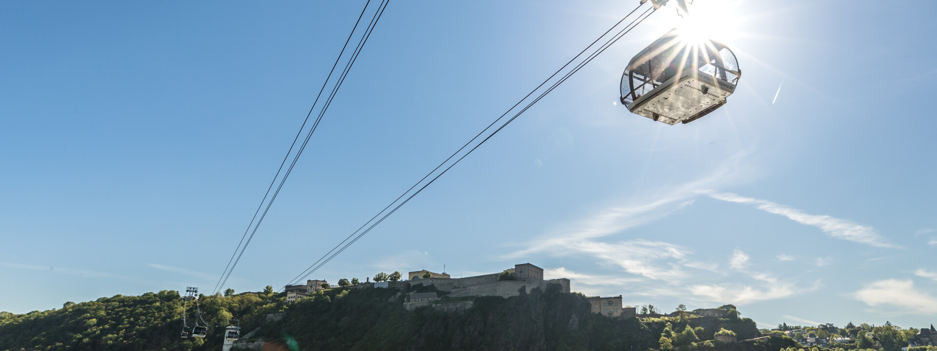 Die Seilbahn Koblenz im Gegenlicht der Sonne mit Rhein im Vordergrund und Festung Ehrenbreitstein im Hintergrund ©Koblenz-Touristik GmbH, Dominik Ketz