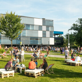 Menschengruppen sitzen verteilt bei der Blaue Stunde vor der Rhein-Mosel-Halle ©Camaze