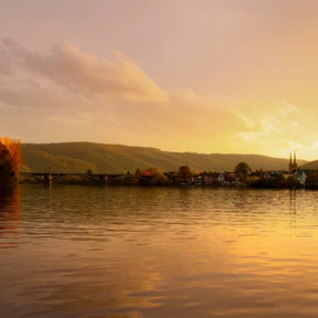Blick über die Mosel bei Sonnenuntergang, im Hintergrund ein kleiner Ort mit Kirchturmspitze