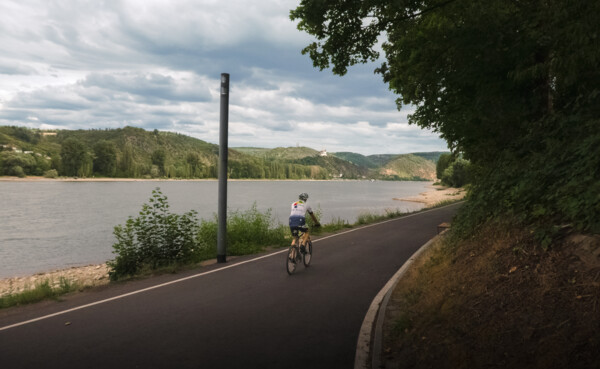 Rennradfahrer auf dem Rheinradweg mit dem Rhein und der Marksburg im Hintergrund ©Ryne & Denise Cook