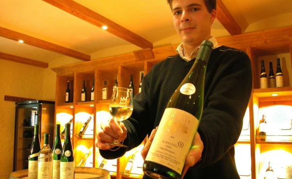 Winzer Toni Müller mit einem Glas und einer Flasche Wein in seinem Weingut