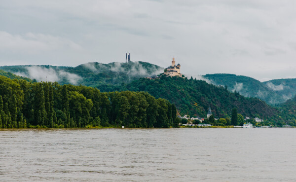 Blick auf die Marksburg vom Rheinufer umgeben von Bergen und Wald mit dem Rhein im Vordergrund © Koblenz-Touristik GmbH, Henry Tornow