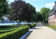 Spazier- und Fahrradweg vor dem Weindorf in den Rheinanlagen umgeben von Statuen, Hecken und Bäumen ©Koblenz-Touristik GmbH